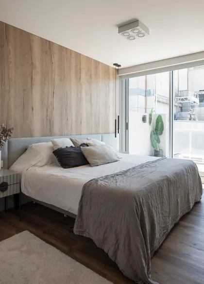 Dormitorio moderno con pared de madera, cama king y luz indirecta — proyecto Depto Arribeños, por Ayelen Mayer Arquitectura, en Buenos Aires